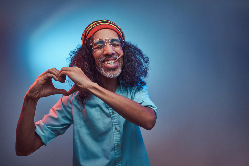 African Rastafarian smokes weed and shows heart symbol and shape with hands.