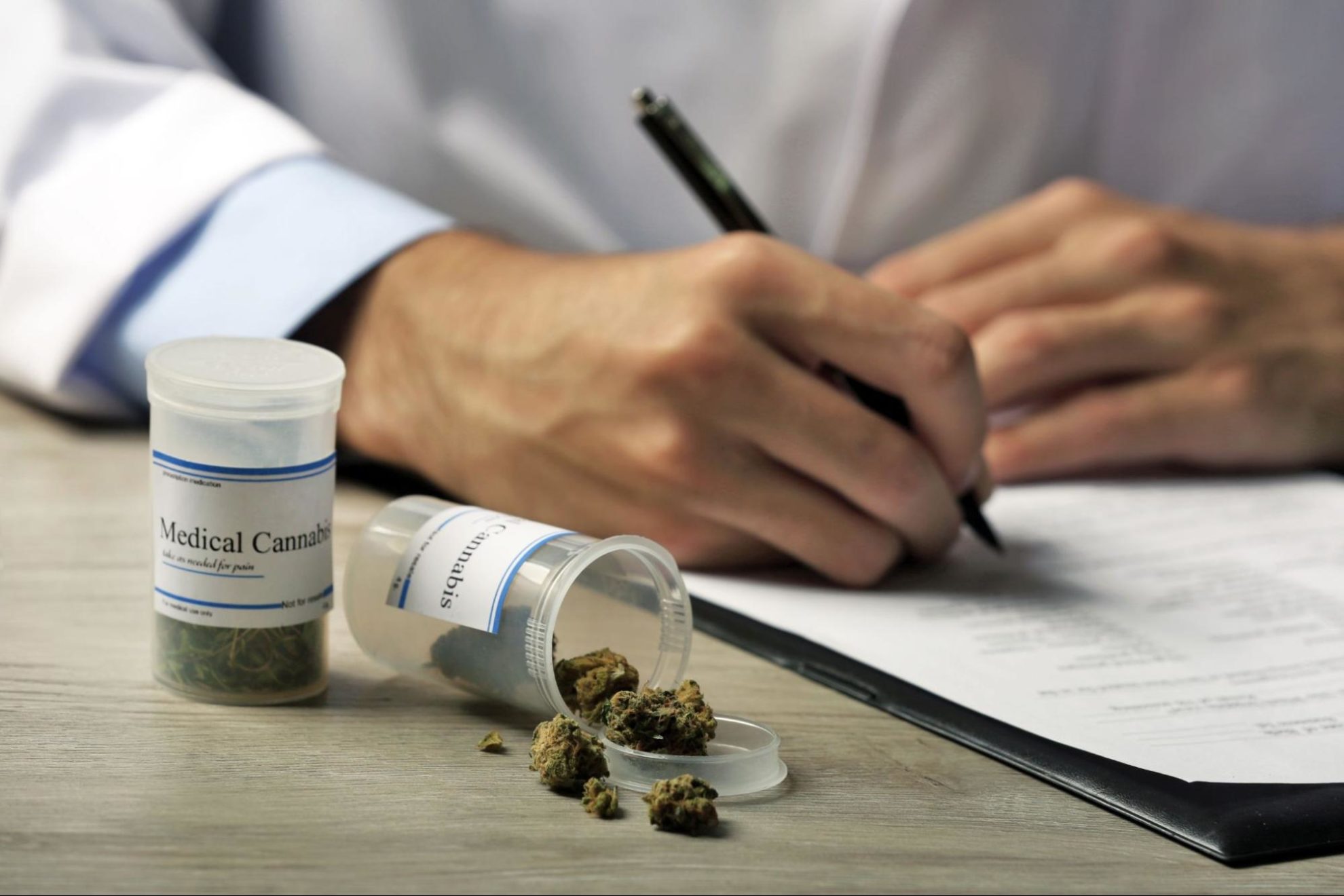Doctor writing on prescription blank and bottle with medical cannabis on table close up