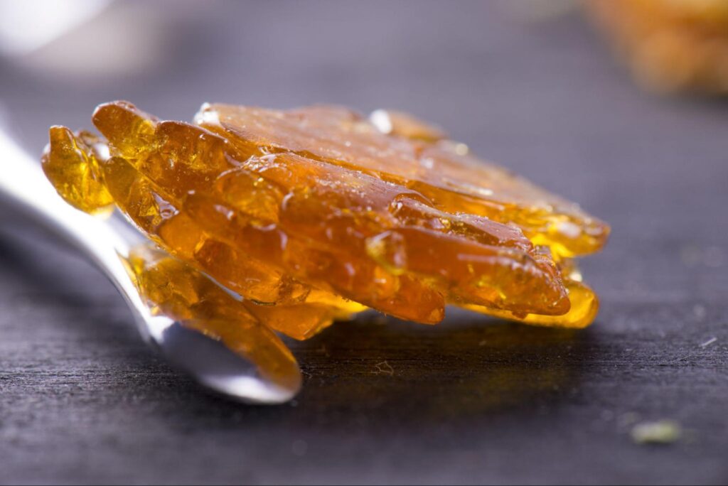 Piece of cannabis oil concentrate aka shatter with dabbing tool over dark background